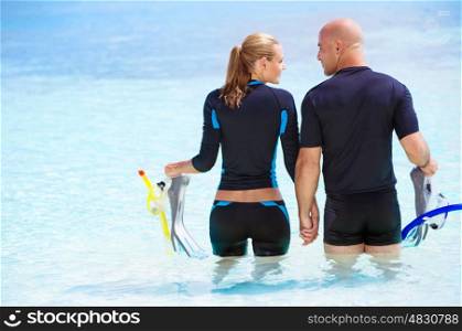 Back side of happy diver couple standing in the water and preparing to dive, enjoying extreme sport and active summer vacation