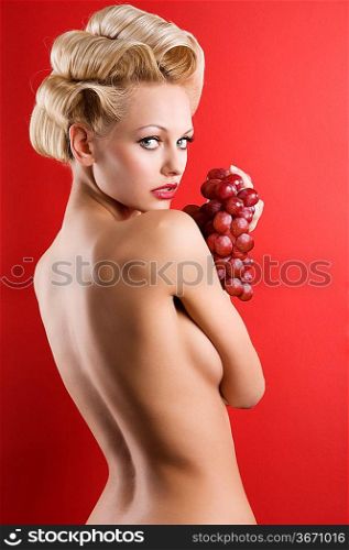 back side portrait of graceful blond nude woman with red grape on red background