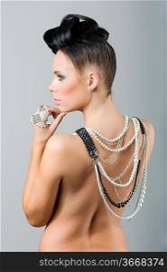 back side portrait of sensual brunette with creative hair style covering her naked shoulder with lots of necklace