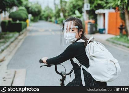 Back to school. asian child girl wearing face mask with backpack biking a bicycle and going to school .Covid-19 coronavirus pandemic.New normal lifestyle.Education concept.