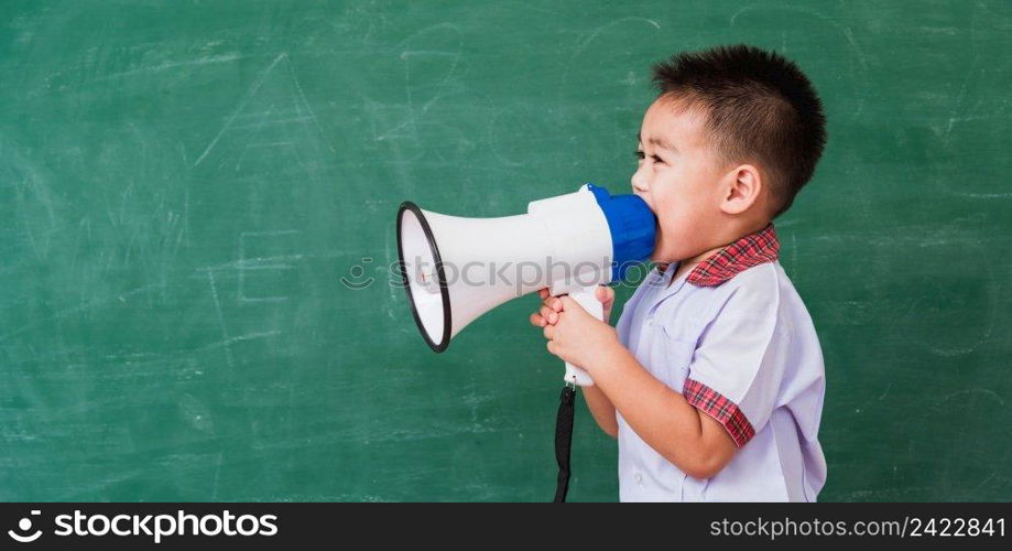 Back to School. Asian funny cute little child boy kindergarten preschool in student uniform speaking through megaphone against on green school blackboard, First time to school education concept