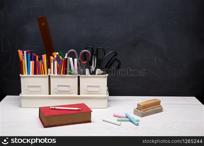 Back to school background with book, pencils, crayons, chalk and other supplies on black chalkboard. Education concept. Copy space