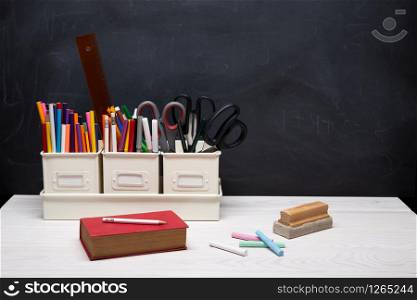 Back to school background with book, pencils, crayons, chalk and other supplies on black chalkboard. Education concept. Copy space