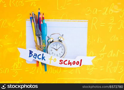 back to school concept - alarm clock and school supplies on ruled paper with back to school text on paper ribbon with math formulas. back to school