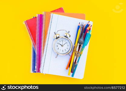 back to school concept - silver alarm clock and school supplies on pile of notebooks. back to school