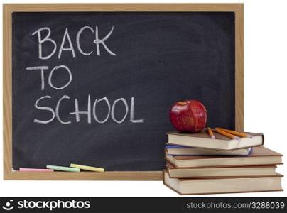 back to school concept - white chalk handwriting on blackboard, stack of old books, red apple and yellow pecils