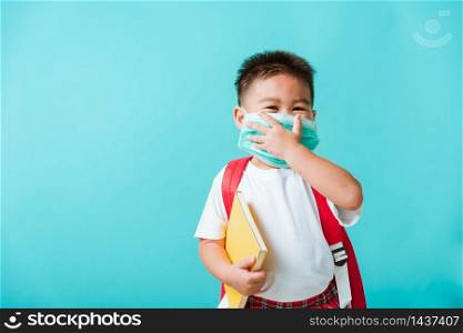 Back to school coronavirus Covid-19 education. Portrait Asian little child boy kindergarten wear face mask protective and school bag hold book before going to school, studio shot isolated background