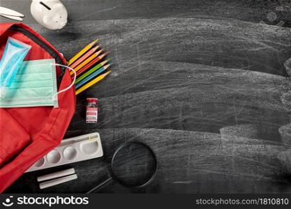 Back to school or college concept. Top view of school supplies stationery, backpack and surgical face mask on blackboard background, Back to start education new normal during outbreak coronavirus