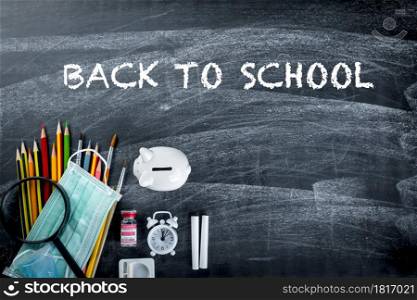 Back to school or college concept. Top view of school supplies stationery and surgical face mask on blackboard background, Back to safe education new normal during outbreak coronavirus pandemic