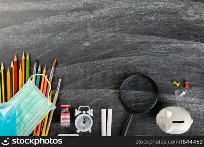 Back to school or college concept. Top view of school supplies stationery and surgical face mask on blackboard background, Back to safe education new normal during outbreak coronavirus pandemic