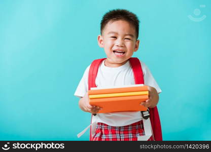 Back to school. Portrait Asian happy funny cute little child boy smiling and laugh holding books, studio shot isolated blue background. Kid from preschool kindergarten with school bag education