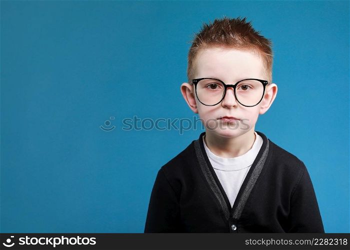 Back to school. portrait of sad little clever school boy in glasses look at the camera, isolated on blue background.. Back to school. portrait of sad little clever school boy in glasses look at the camera, isolated on blue background