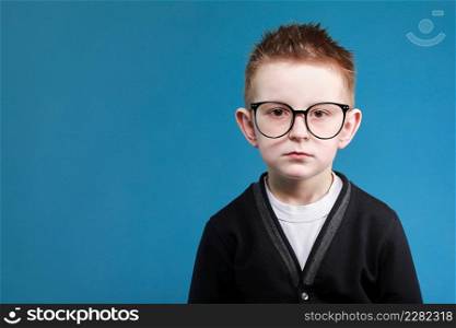 Back to school. portrait of sad little clever school boy in glasses look at the camera, isolated on blue background.. Back to school. portrait of sad little clever school boy in glasses look at the camera, isolated on blue background