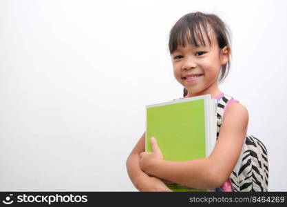 Back to school. Smiling little girl carrying a backpack holding books looking at the camera on a white background with copy space. Girl glad ready to study.