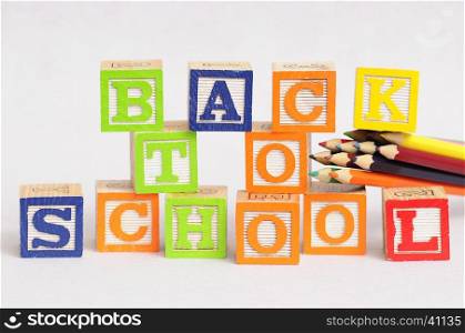 Back to school spelled with alphabet blocks displayed with coloring pencils on a black background