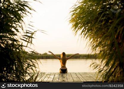 Back view at young woman in bikini on wooden pier by river