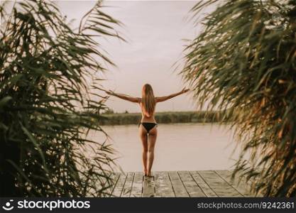 Back view at young woman in bikini on wooden pier by river