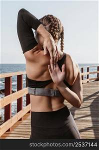 back view athletic woman outdoors by beach stretching her arms