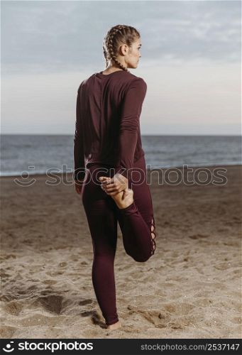 back view athletic woman stretching by beach 2