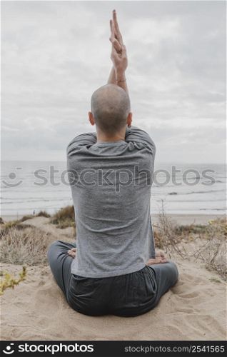 back view man outside meditating while doing yoga