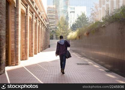 Back view of a attractive young man holding shoulder bag walking through the city