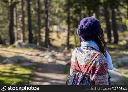 Back view of a backpacker woman standing in a forest trail while looking away