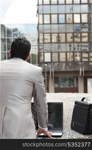 Back view of a businessman standing outside with computer and briefcase