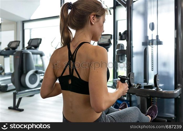 Back view of a fitness woman doing heavy athletic workout in the gym.