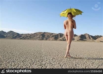 Back view of a naked woman with umbrella walking on barren landscape
