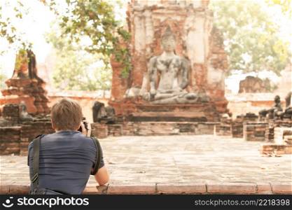 Back view of a tourist man taking pictures with a digital camera at an ancient Buddhist temple in Ayutthaya Historical Park, UNESCO World Heritage Site, Phra Nakhon Si Ayutthaya, Thailand. Focus on tourist man.