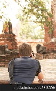 Back view of a tourist man taking pictures with a digital camera at an ancient Buddhist temple in Ayutthaya Historical Park, UNESCO World Heritage Site, Phra Nakhon Si Ayutthaya, Thailand. Focus on tourist man.