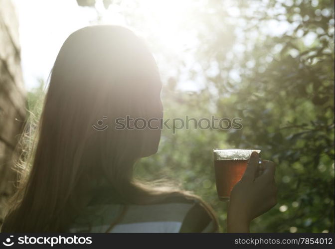 Back view of a woman with glass cup of tea against bright evening sun flare