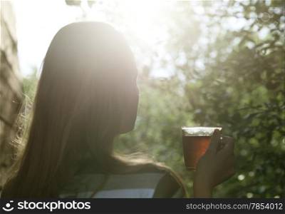 Back view of a woman with glass cup of tea against bright evening sun flare