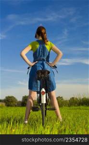 Back view of a womanl over her bicycle, in a green meadow