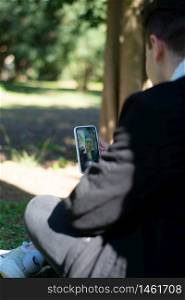 Back view of a young teenager student sitting on campus while using a mobile phone