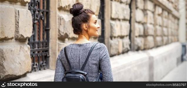 Back view of a young woman with a backpack walks in a European city. Young woman walks with backpack