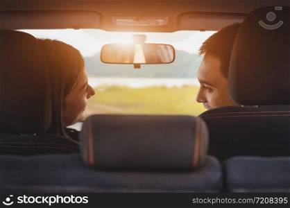 Back view of Asian couple looking each other in hatchback car at camping picnic place with green meadow and mountain. People lifestyles and transportation concept. Valentines day and honeymoon wedding