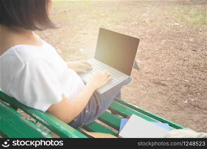 Back view of asian mid adult entrepreneur businesswoman sit in park using laptop for work outside office in casual dress looking notebook with thinking and concentrate in park.