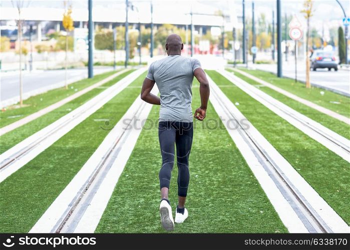 Back view of black man running in urban background. Male doing workout outdoors.
