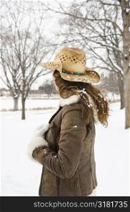 Back view of brunette woman with long hair wearing straw cowboy hat outdoors in the snow.