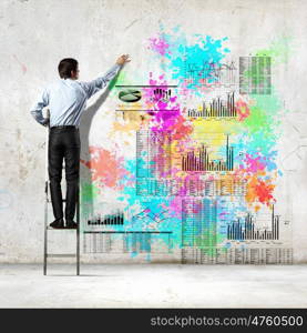 Back view of businessman. Back view of businessman drawing colorful business ideas on wall