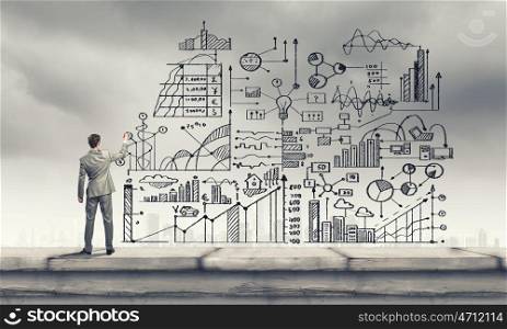 Back view of businessman drawing business sketches on wall
