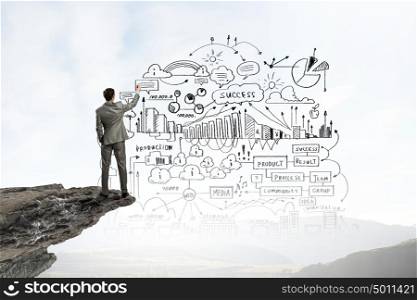 Back view of businessman drawing business sketches on wall