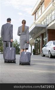 Back view of businesspeople walking with luggage outside hotel