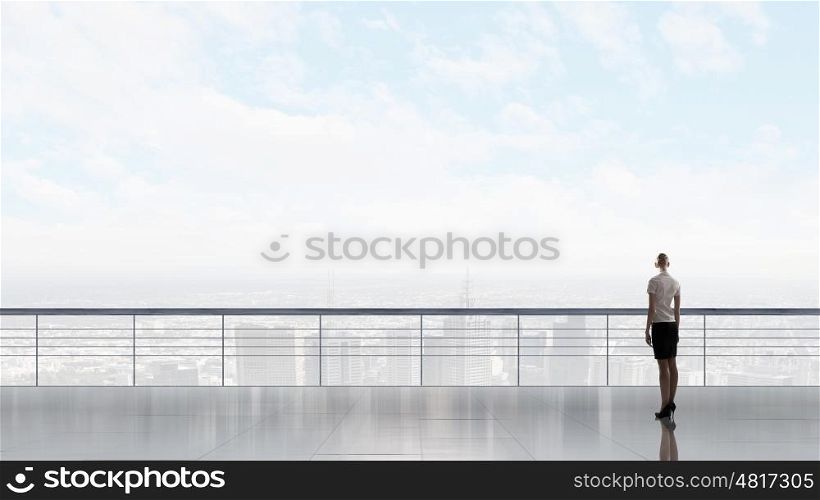 Back view of businesswoman standing on roof looking at city. On top of business
