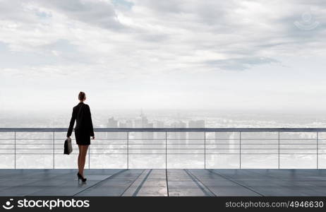 Back view of businesswoman standing on roof looking at city. On top of business