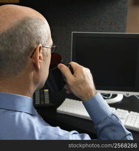 Back view of Caucasian middle-aged businessman drinking from coffee cup sitting at desk looking at computer.