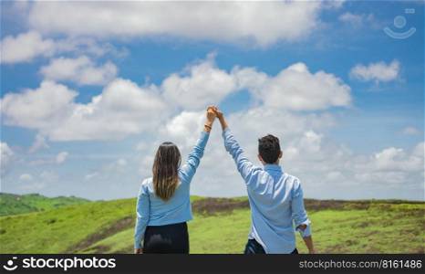 Back view of couple on the hill with hands raised to the sky, Happy couple in the field raising hands to the sky, Concept of a happy and free couple in the field
