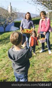 Back view of cute boy taking a photo with electronic tablet to family with fresh organic apples in a wicker basket after harvest. Three different generations concept.. Boy taking photo to family with apples in basket