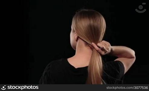 Back view of cute woman with pony tail letting her hair down isolated on black background. Blonde female with amazing long hair fluttering with wind. Slow motion.